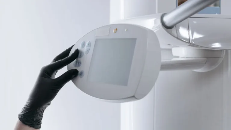 Close-up of gloved hand operating dental x-ray machine in clinical setting.