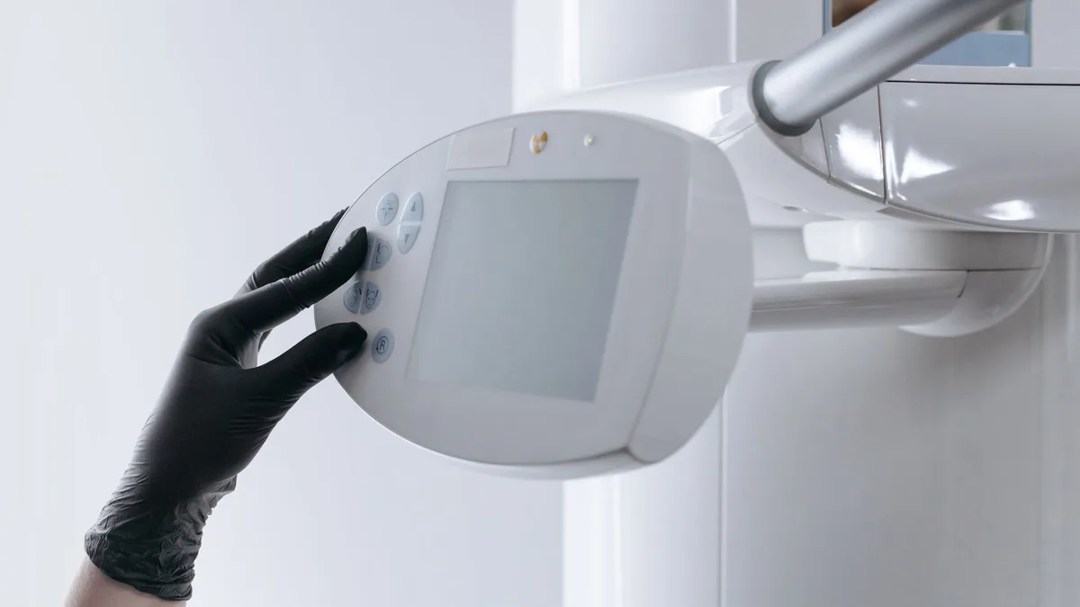 Close-up of gloved hand operating dental x-ray machine in clinical setting.