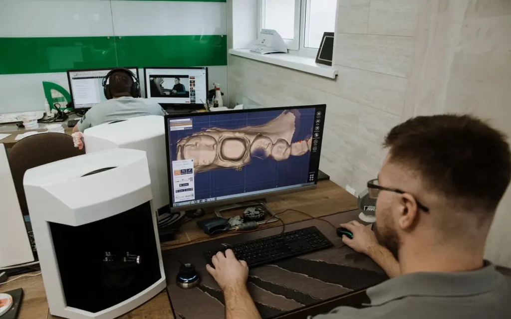 Technik projektuje uzupełnienie w programie CAD, obok stoi skaner laboratoryjny