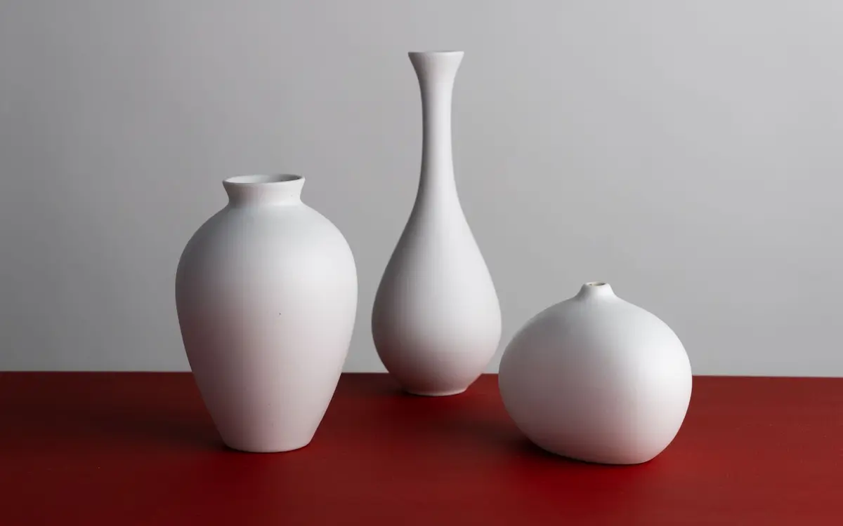 Trzy matowe porcelanowe wazony na czerwonym blacie - biel, faktura i półmat porcelany