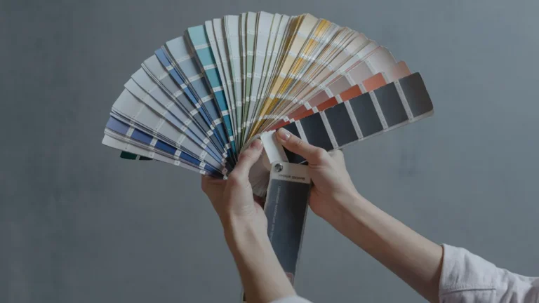 Hands holding a colorful fan of swatches on a gray backdrop, ideal for design themes.