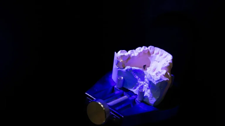 From above of white dental impression for creating denture placed on table in darkness illuminated by blue light against black background