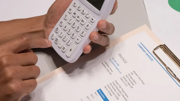 Close-up of hands using a calculator next to a company invoice, depicting a financial calculation concept.