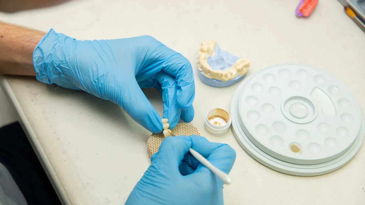 From above of crop anonymous orthodontist in latex gloves making fake teeth for denture in modern dental clinic