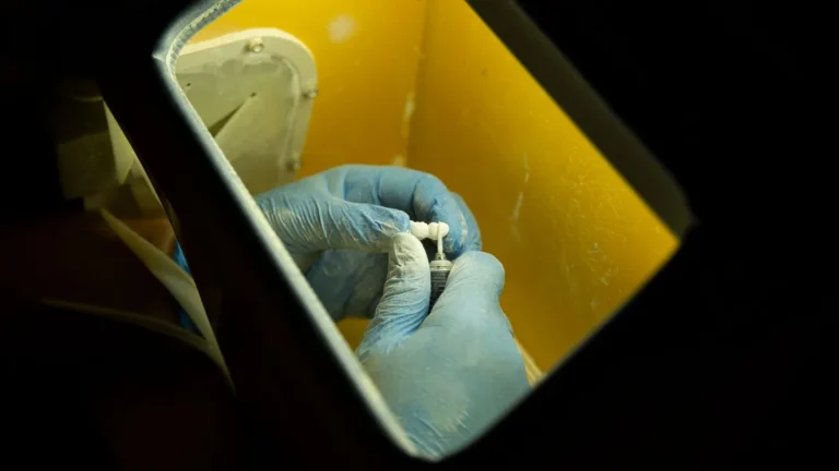 From above of crop anonymous master in latex gloves creating dental implant using medical equipment against black background
